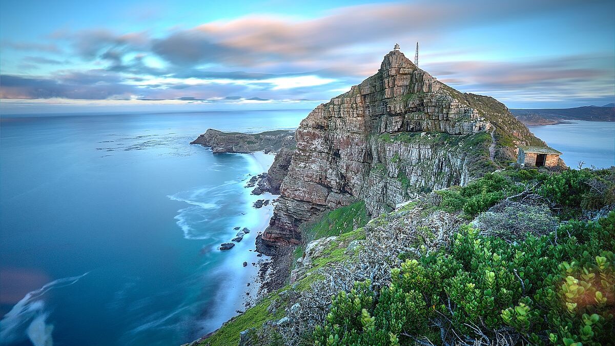 Using AI to plan a safari - Cape Point South Africa as time stands still - slight movement in the water and clouds as the sun rises in the back. There's a lighthouse on top of the cliff which serves to warn passing ships that there's land.