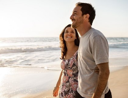 Loving young couple looking at each other while walking arm in arm together along a sandy beach